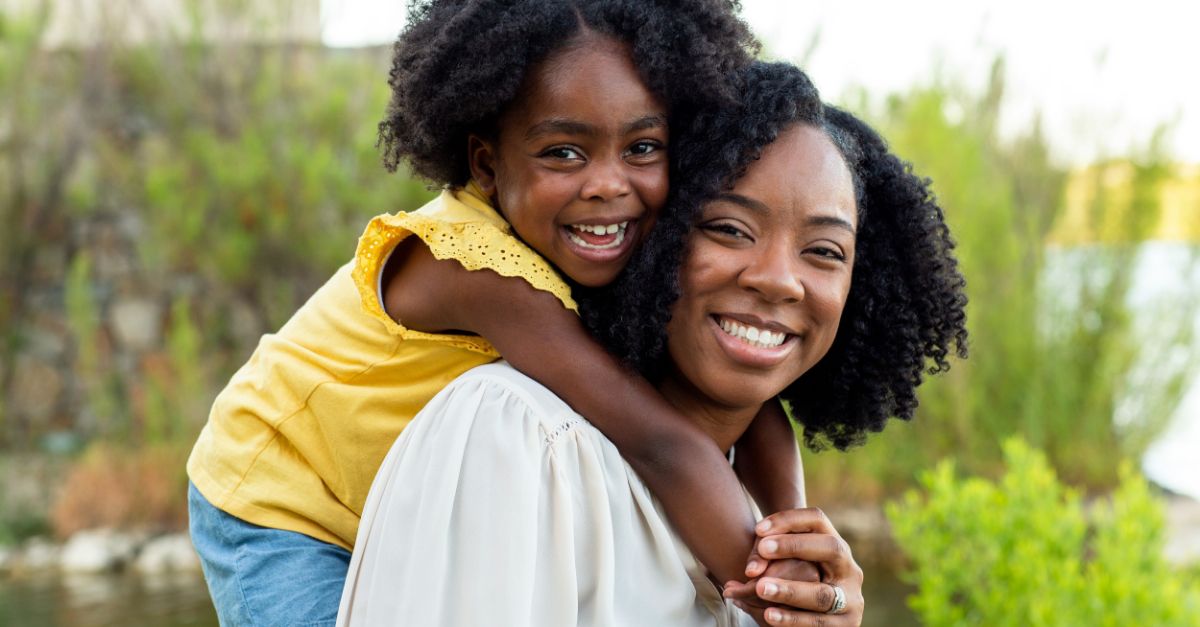 A Black mother holding her daughter on her back